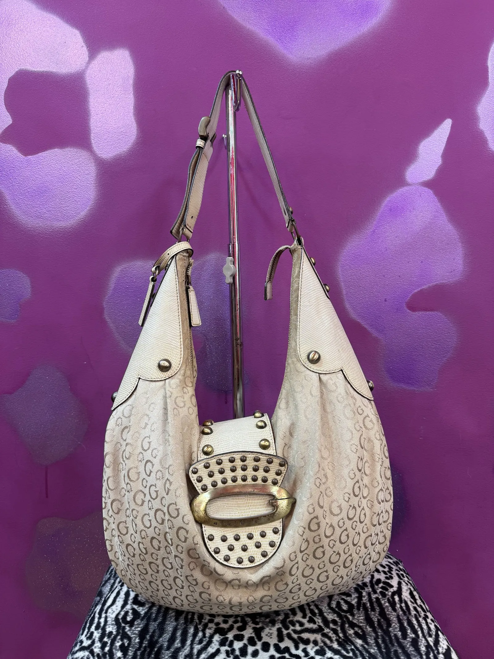 Bolso blanco con tachuelas doradas sobre una pared morada