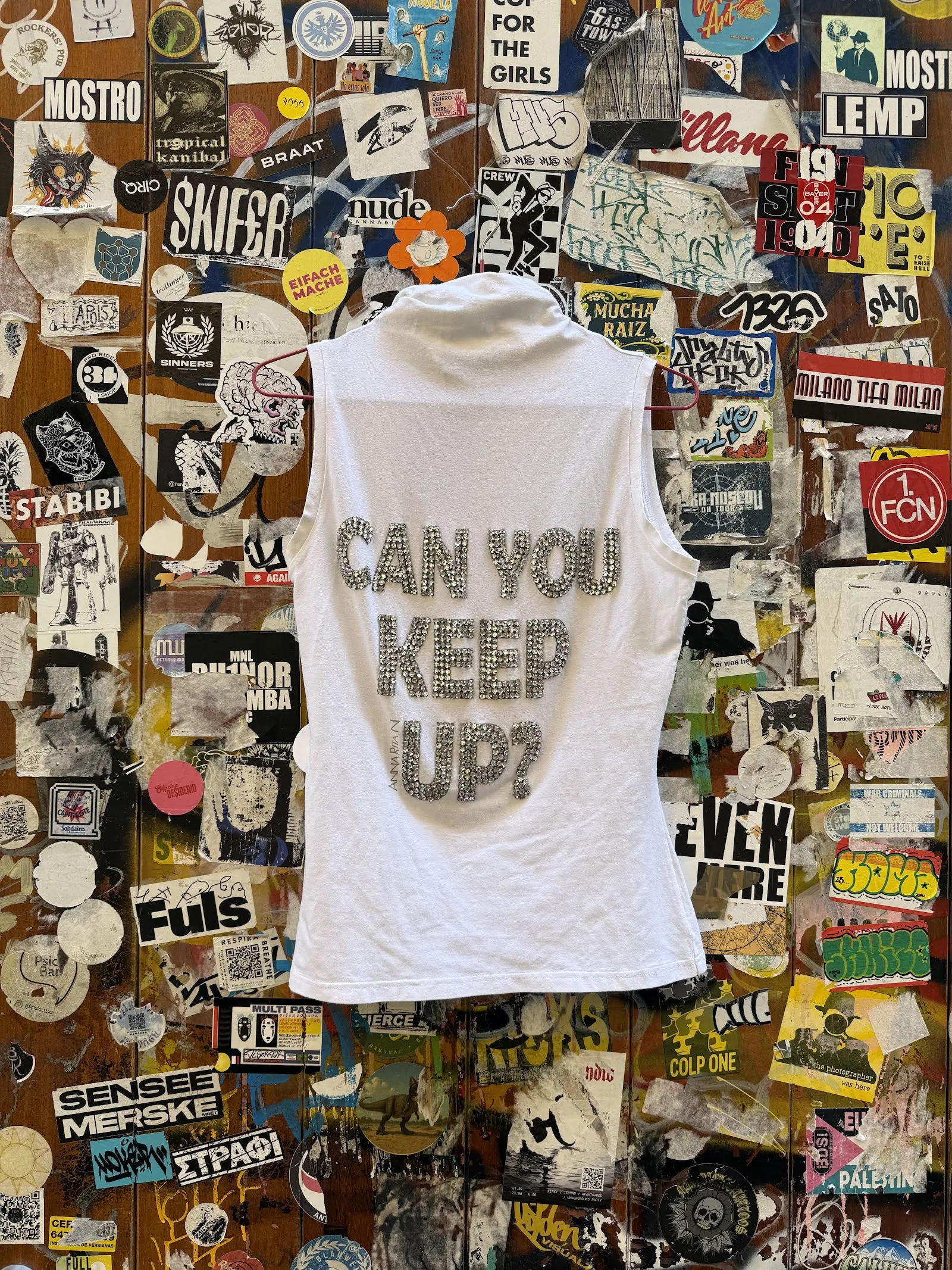 Top blanco con la frase «Can you keep up?» sobre una pared de pegatinas