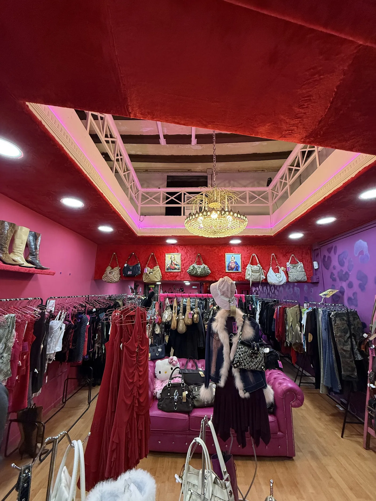 Interior de la tienda: paredes y techo fucsia, lámpara de araña y perchas llenas